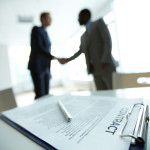 Image of business contract on background of two employees handsh